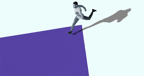 A high-angle view of a man running against a flat background of colors, crossing the line between an area of desaturated blue and a large rectangle of deep purple that extends beyond the frame