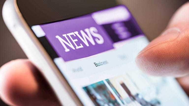 Newsroom: a closeup of a thumb scrolling on a mobile device, with a purple and white "News" header visible on screen while the rest of the content is washed out or out of focus